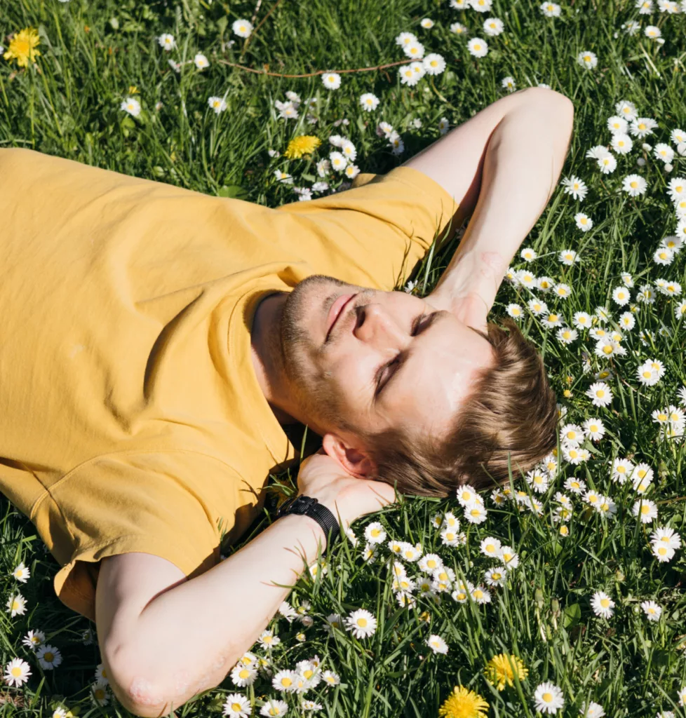 Young man laying in green grass with flowers.